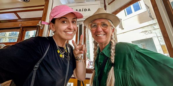 A smiling mother and adult daughter sitting together on a tram with the daughter making a peace sign, representing the joy of mother's day gifts and heartfelt card messages with Photobox.