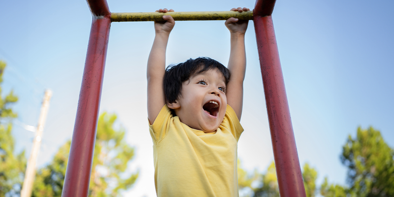 A young boy smiles while hanging off monkey bars in a playground, capturing the last days of summer before Photobox's back-to-school tips for a fun and organised school year.