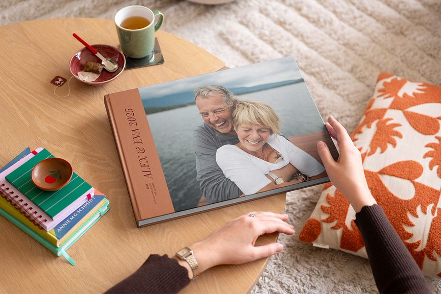 Close-up of a 2025 year in review photo book cover featuring a happy older couple, with a woman's hands about to open the yearly photo album.