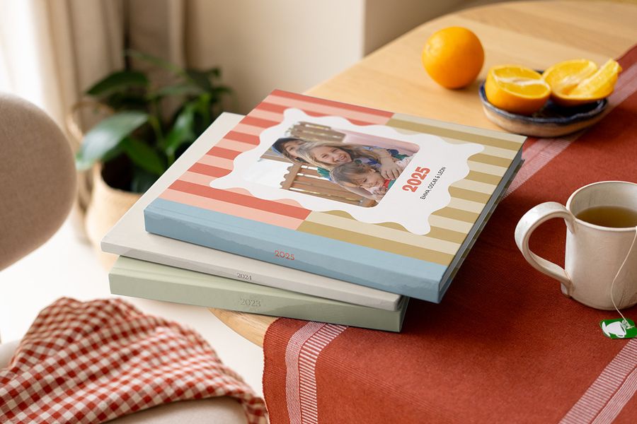 A stack of colourful, patterned Photobox yearly photo books and annual photo albums with varying designs, sitting on a coffee table.
