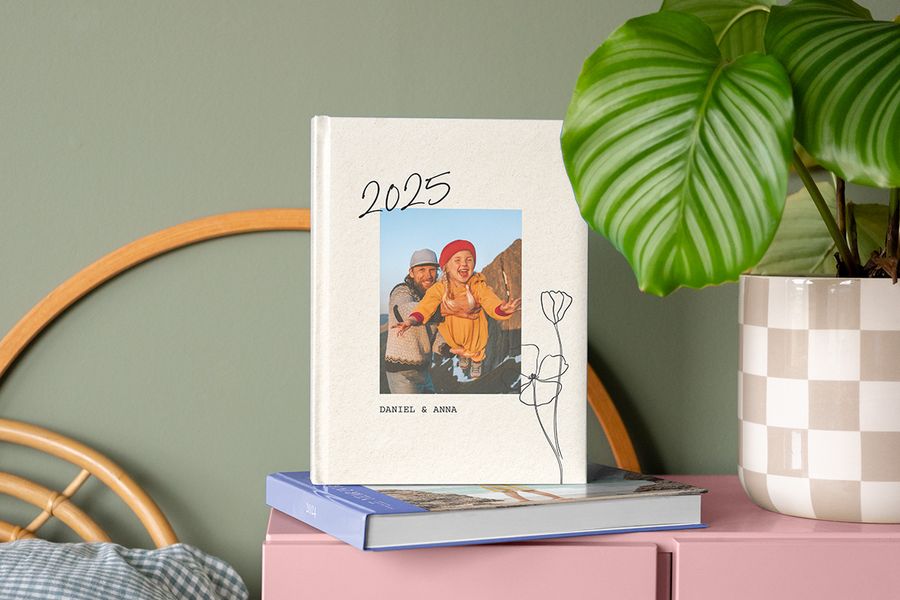 A 2025 annual photo book showing a father and daughter on the cover, resting on top of the 2024 yearly photo album on a bedside table.