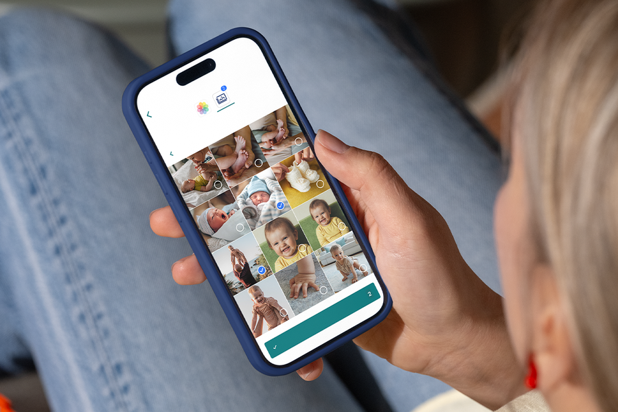 A hand selecting baby photos on a smartphone to create a personalised first year photo album with Photobox.