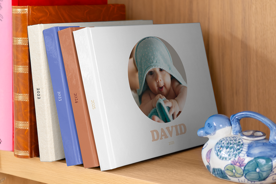 A series of photobooks spanning different years, such as a babys first year photo book, arranged on a bookcase.