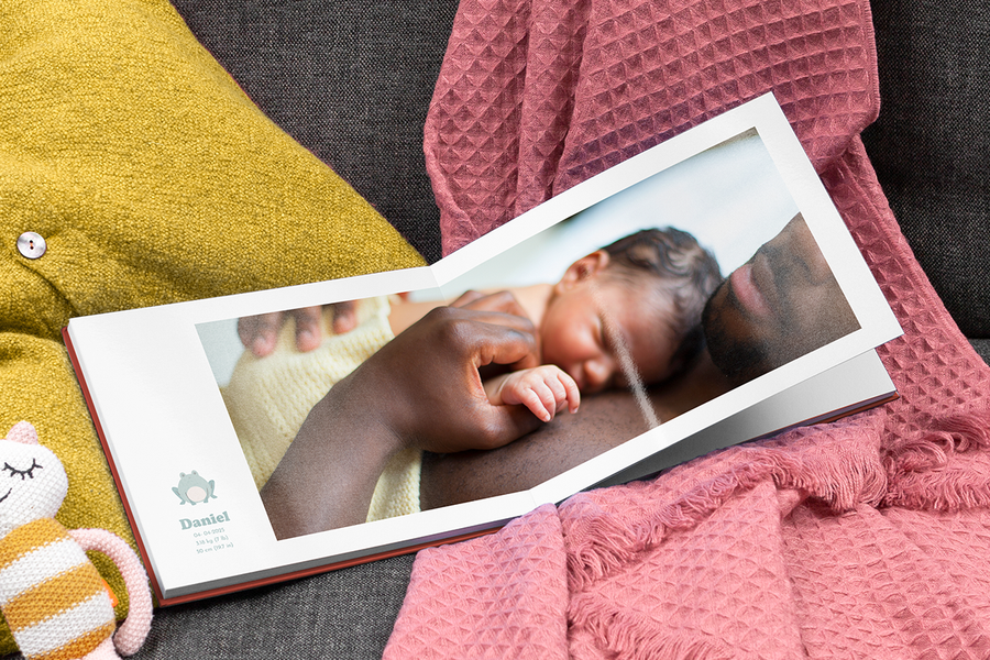 A father holding his newborn baby in an open my first year photo book featuring the baby's birth stats.