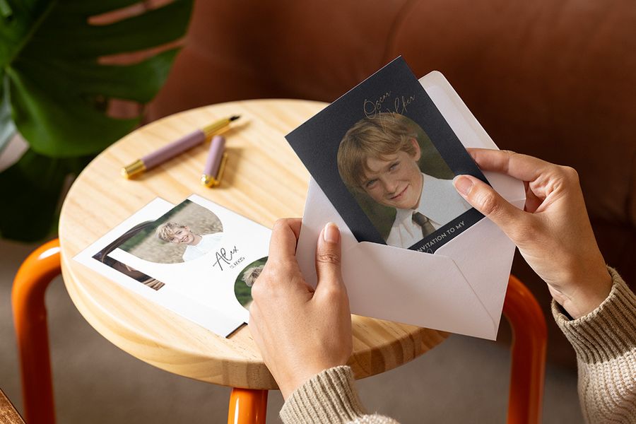 Someone looking at a boy's first holy communion invitations from Photobox with several more invitations displayed on a table behind them.