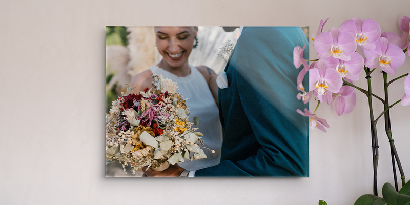 Wedding wall art by Photobox showing a smiling bride holding a bouquet, displayed on a wall next to an orchid.