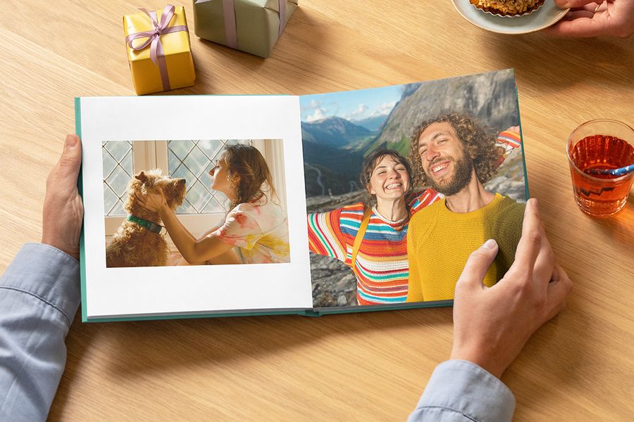 An open hardback birthday photo book from Photobox showing a woman with her dog and a smiling couple on their travels, perfect for a birthday memory book.