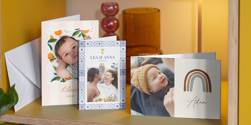 A selection of personalised cards on a shelf, featuring two baby announcements and a personalised wedding card, showing how easy it is to create your own card with Photobox.