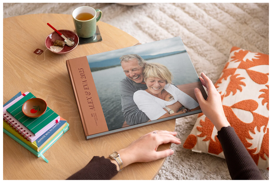Someone about to open a closed premium layflat 2025 photo book on a coffee table, with a smiling older couple on the front cover from Photobox.