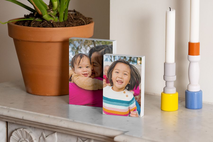 Two photo blocks featuring a woman with a baby and a young girl displayed on a fireplace mantel next to a plant and candlesticks, showing renter-friendly decor with Photobox.