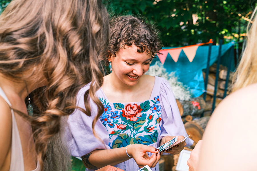 A woman in formal dress at a wedding holding photo prints for a secret wedding mission game, inspiring Photobox wedding games and wedding table games for guests.