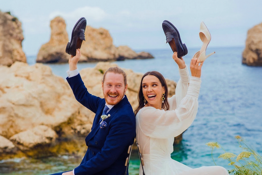 A bride and groom on the beach on their wedding day playing the wedding shoe game, inspiring Photobox wedding games and fun wedding games for guests.