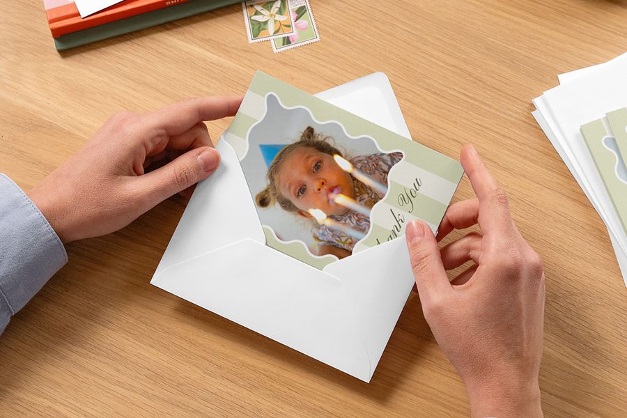 Hands placing a personalised child’s thank you card into an envelope, inspiring Photobox children’s party ideas and personalised thank you cards after a children’s birthday party.
