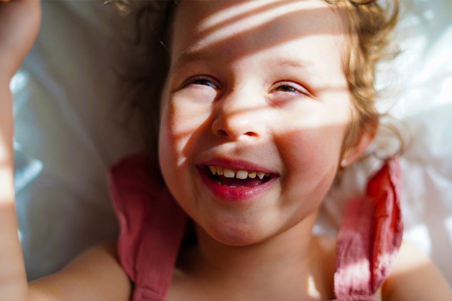 A smiling little girl with sunlight and soft shadows across her face, inspiring Photobox tips on how to take good pictures in bright sunlight.
