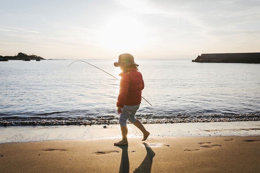 A child standing on the beach by the sea with a strong shadow behind them, illustrating the dramatic effect of silhouette photography in sunlight.