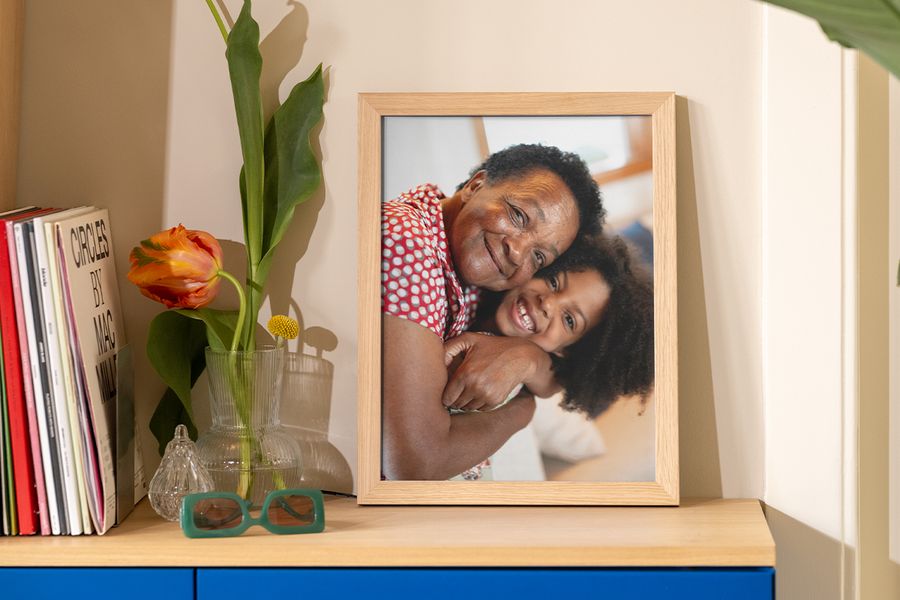 A framed photo of a grandmother and granddaughter hugging sits on a table beside books, a magazine and a funky vase, inspiring frame trends and affordable ways to elevate your wall decor.