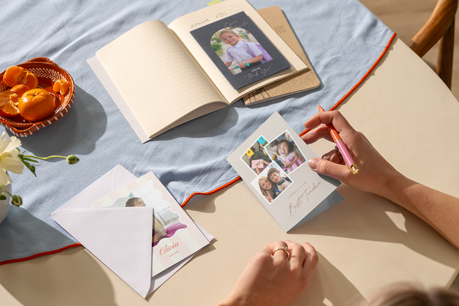 A woman’s hand rests on a table, ready to write in a personalised Photobox thank you teacher card featuring several photos of happy children.