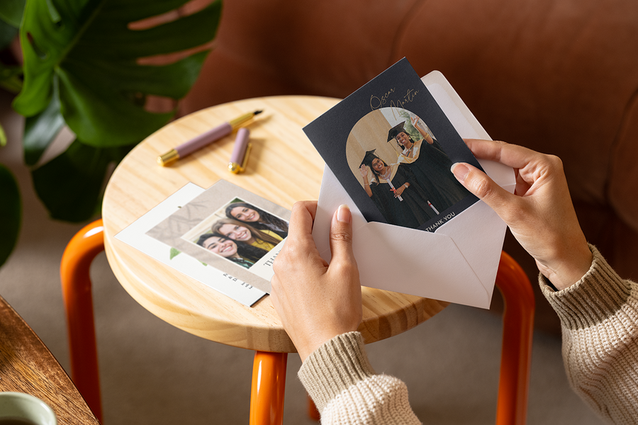 Hands placing a personalised Photobox thank you teacher card featuring graduates on the front into an envelope.
