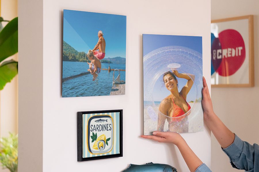 A gallery wall of personalised Photobox wall art shows a smiling woman at the beach, a man and boy jumping into the sea, and a sardine tin illustration, inspiring home decor for summer and bright summer wall decor ideas.