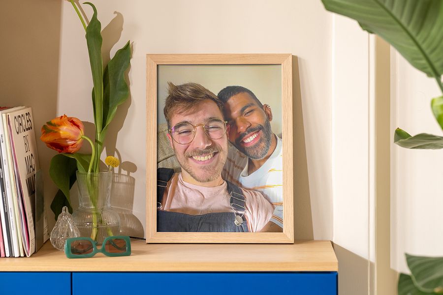 A framed photo of two men taking a selfie in the sun sits on a sideboard beside a vase, sunglasses and a magazine, inspiring summer room decor and easy summer home decor ideas.