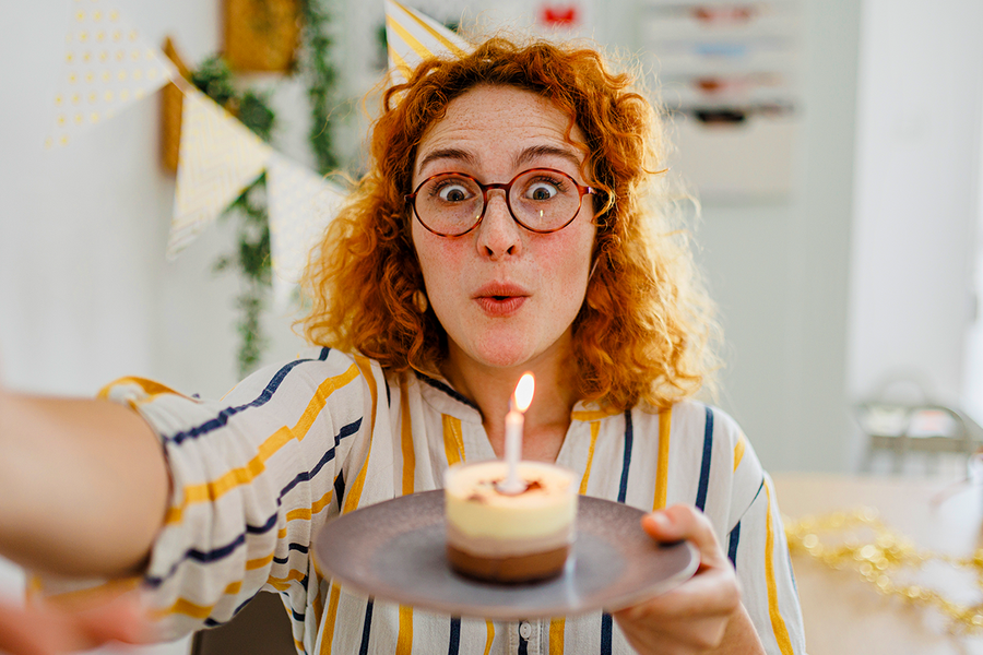 A woman with ginger curly hair holds a cupcake with a candle, inspiring happy birthday wishes for a coworker and birthday card ideas from Photobox.