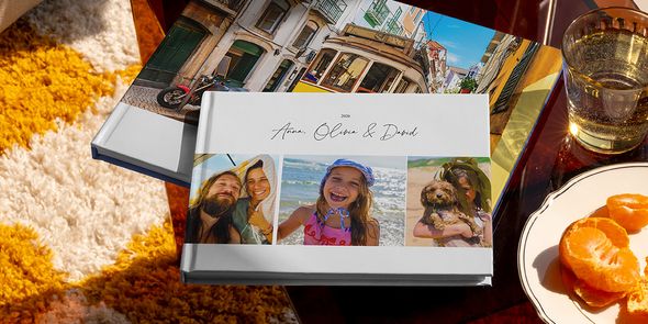 Two different Photobox travel photo books are displayed together, including a landscape holiday photo book with family travel photos on the cover and another with a tram holiday shot, showing different personalised travel photo book ideas.