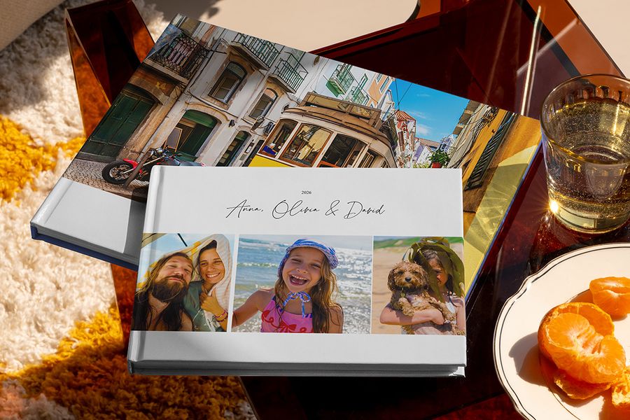 Two different Photobox travel photo books are displayed together, including a landscape holiday photo book with family travel photos on the cover and another with a tram holiday shot, showing different personalised travel photo book ideas.