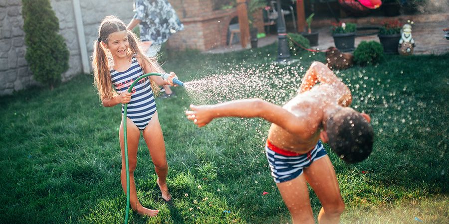 A girl and a boy play in the garden with a garden hose, enjoying a fun family staycation moment featured in Photobox's staycation ideas guide.