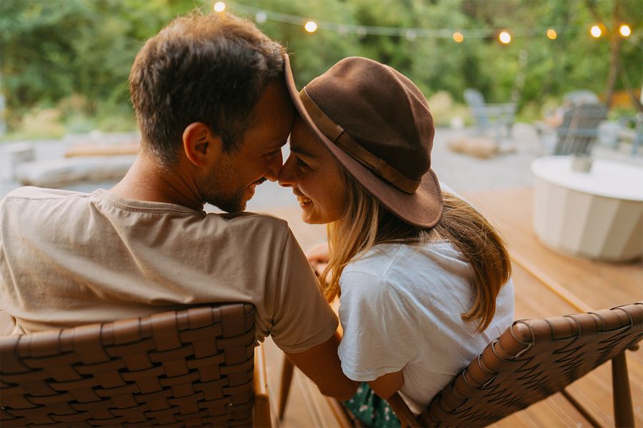 A man and a woman sit nuzzling together in a garden strung with fairy lights, a romantic moment from Photobox's staycation ideas for couples.