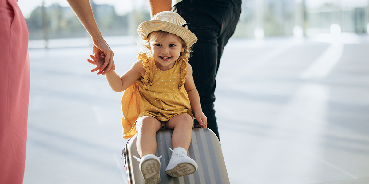A little girl sits on a suitcase being pulled along, capturing a playful family travel moment and inspiring travelling with children and family travel tips from Photobox.