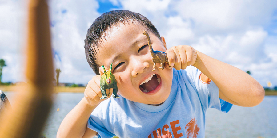 A little boy holds two plastic dinosaur toys, illustrating Photobox family travel tips and simple children’s travel bag ideas for keeping kids entertained on holiday.