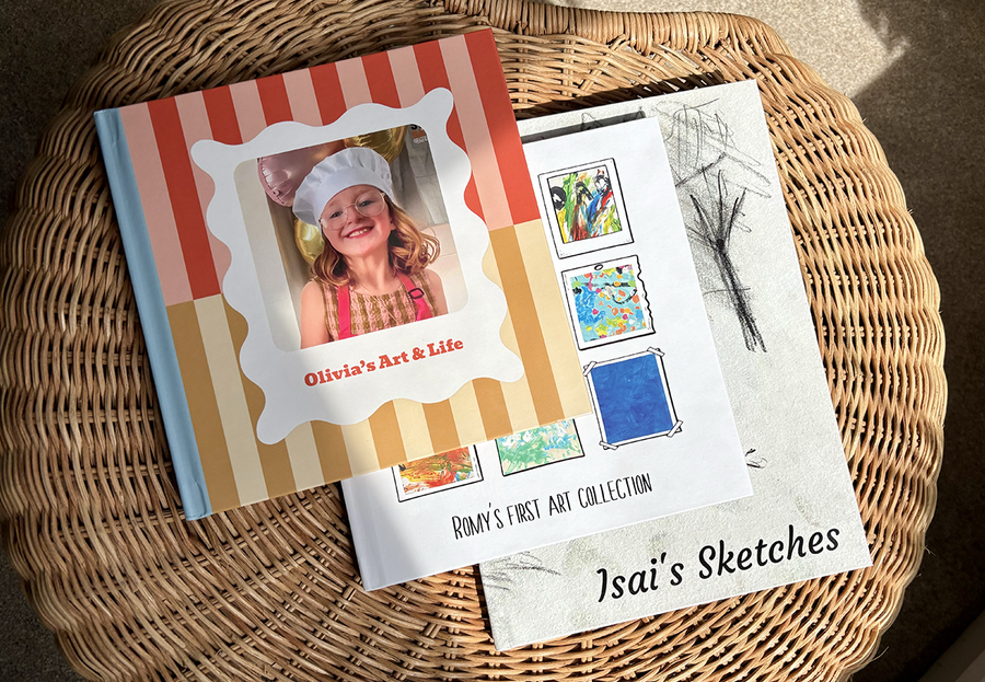 Three children's photo books are stacked on a coffee table, each showcasing artwork from a different age group, from young children's paintings to teenage sketches, highlighting the benefits of a Photobox children's photo album.