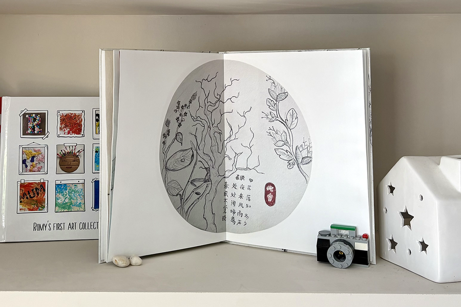 An open children's photo book shows a full-page spread of tree sketches with text, next to a closed photo book featuring a scrapbook-style cover with various examples of kids' artwork, illustrating the meaningful keepsake a Photobox children's photo album creates.