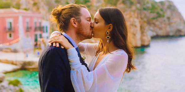 A bride and groom kiss on their wedding day against a Mediterranean-style backdrop, capturing the romance of 2026 wedding trends and personalised wedding style from Photobox.