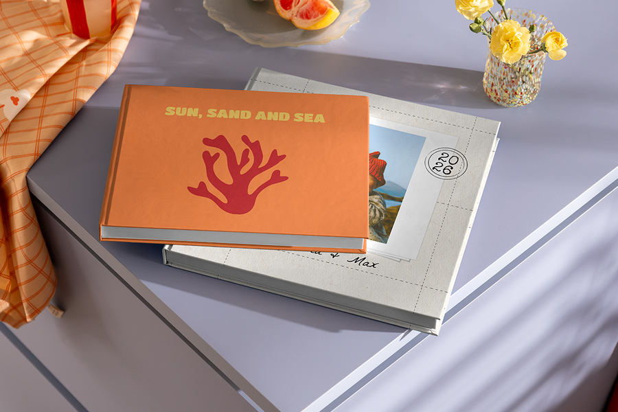 Two photo books are stacked on top of each other, with the top book featuring a coral design and the title 'Sun, Sand and Sea', illustrating Photobox's beach holiday photo album title ideas.