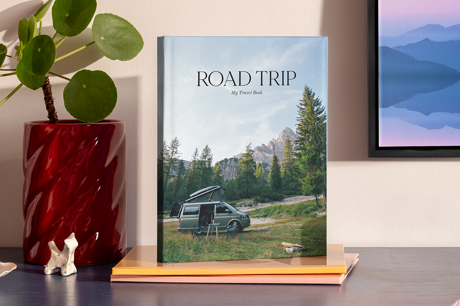 A large portrait photo book features a picture of a camper van in a mountainous, national park style landscape, illustrating Photobox's road trip photo album title ideas.