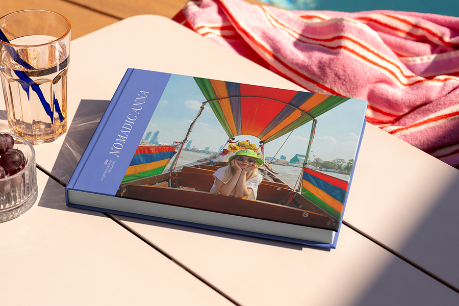 A large landscape travel photo book titled 'Nomadic Anna' sits on a table, featuring a photo of a girl on her travels on the cover, illustrating Photobox's travel photo album title ideas.