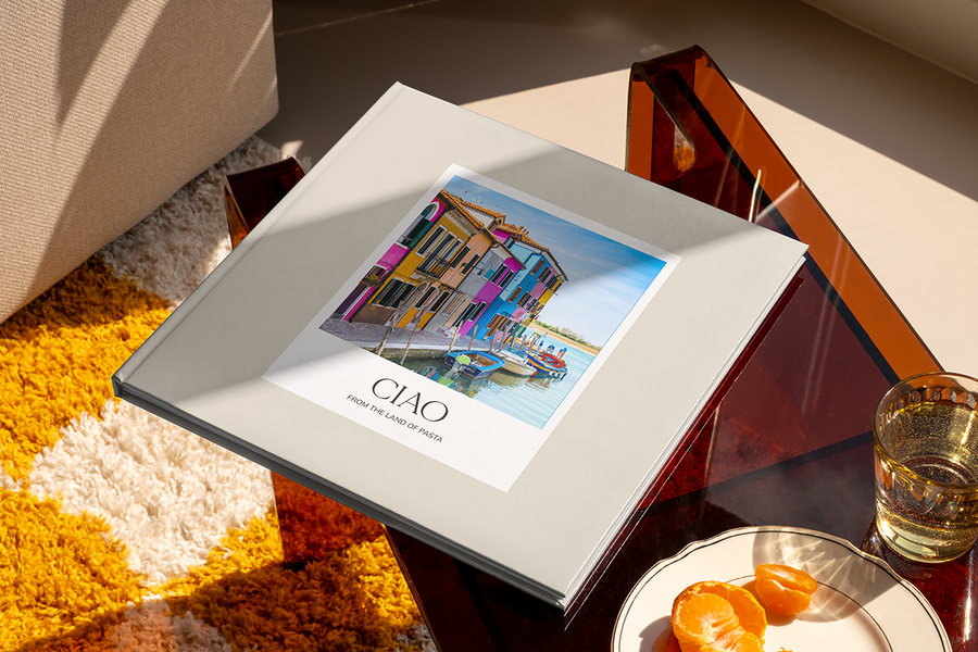 A photo book featuring a canal and colourful houses in Italy on the cover is titled 'Ciao from the Land of Pasta', illustrating Photobox's city travel photo album title ideas.