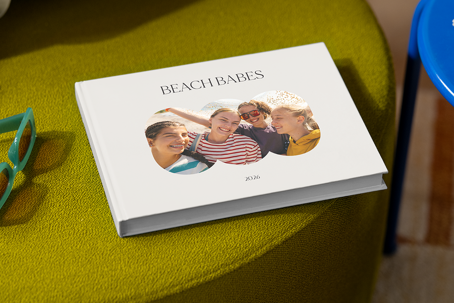 A photo book featuring four smiling girls on the cover is titled 'Beach Babes', illustrating Photobox's travels with friends photo album title ideas.