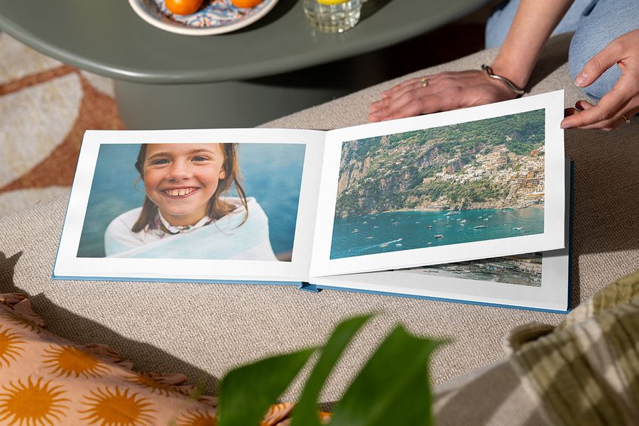 An open photo book shows a girl smiling by the sea on one page and a beach landscape shot on the other, illustrating Photobox's Holiday Escape design with immersive full-page photography.