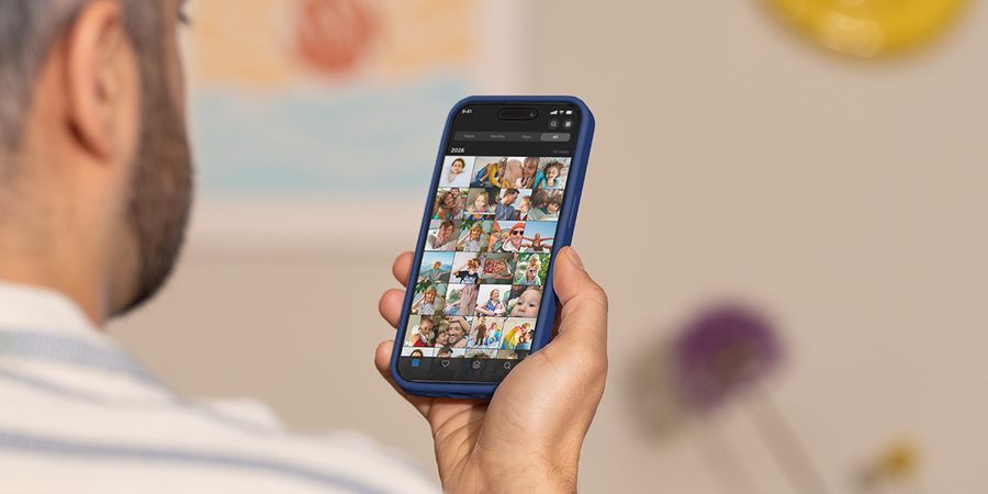A man holds up his phone, scrolling through his camera roll, illustrating Photobox's guide to managing photo overload and culling tips.