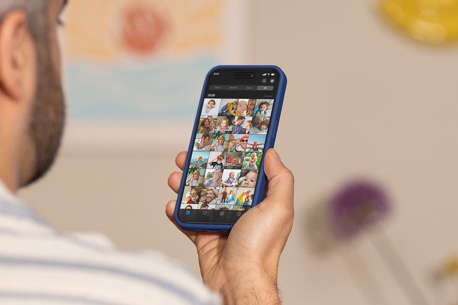 A man holds up his phone, scrolling through his camera roll, illustrating Photobox's guide to the best tools for organising photos.