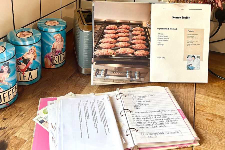 Sarah's open personalised recipe book shows a recipe for her Nene's kofte, placed in front of an old binder open to reveal handwritten family recipes, both resting on a kitchen counter, illustrating how she gathered generations of recipes into one book.