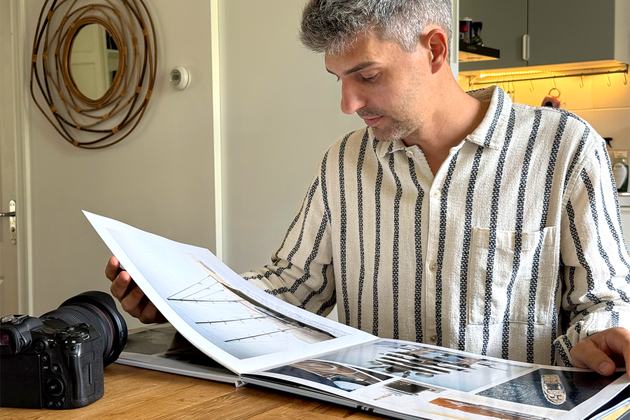 Charl van Rooy sits in his kitchen looking down at his open portfolio, with his camera beside him on the table, illustrating Photobox's guide to building a photography portfolio photo book.