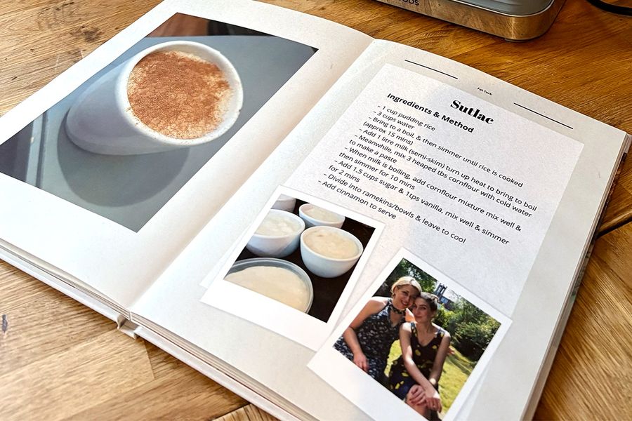 Sarah's open recipe book lies on the kitchen counter, showing its layflat photo book format, with images of Turkish rice pudding on the left page and her family's corresponding recipe on the right, illustrating Photobox's tip to choose a layflat design that's easy to cook from.