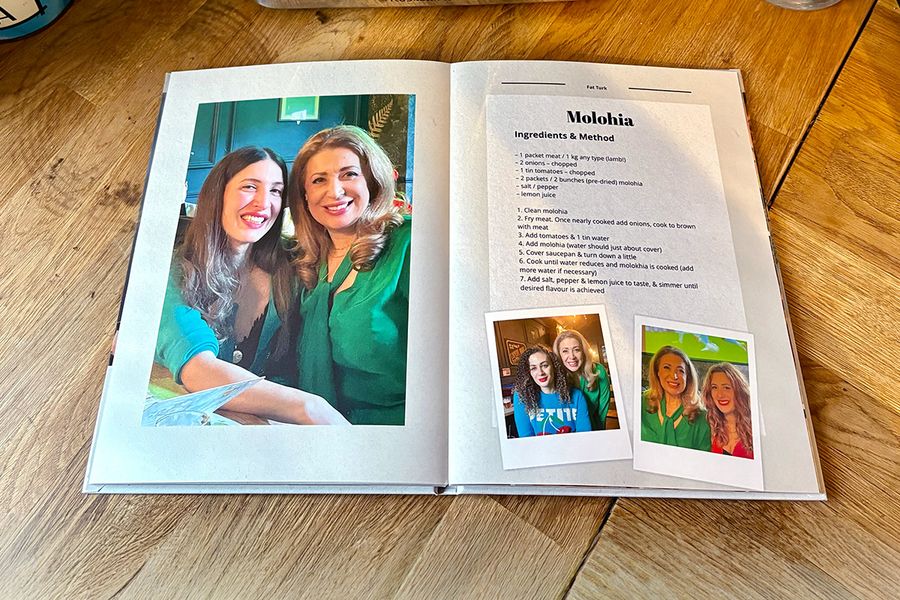 A spread from Sarah's personalised recipe book shows a recipe for molohia, accompanied by family photographs instead of a picture of the dish, illustrating Photobox's tip to include personal photos that make a recipe book truly meaningful.