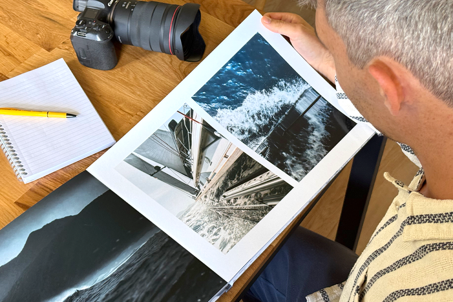 Photographer Charl van Rooy looks down at his portfolio, with his camera and a notebook on the table beside him, illustrating Photobox's tips for choosing the best templates and layouts for a photography portfolio.