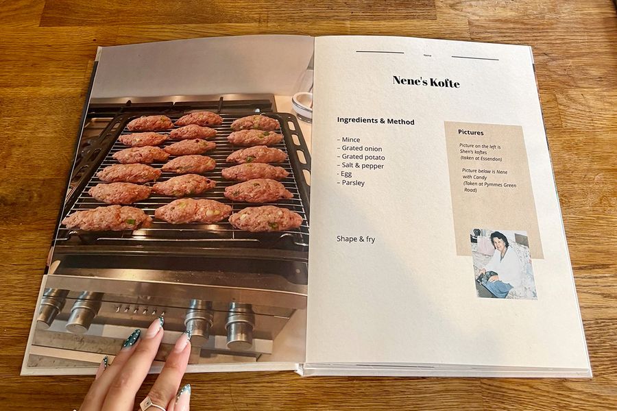 An open spread from Sarah's recipe book shows her Nene's kofte recipe, with a woman's manicured hand resting on the book on a wooden counter, illustrating Photobox's final checklist tips before printing a personalised cookbook.