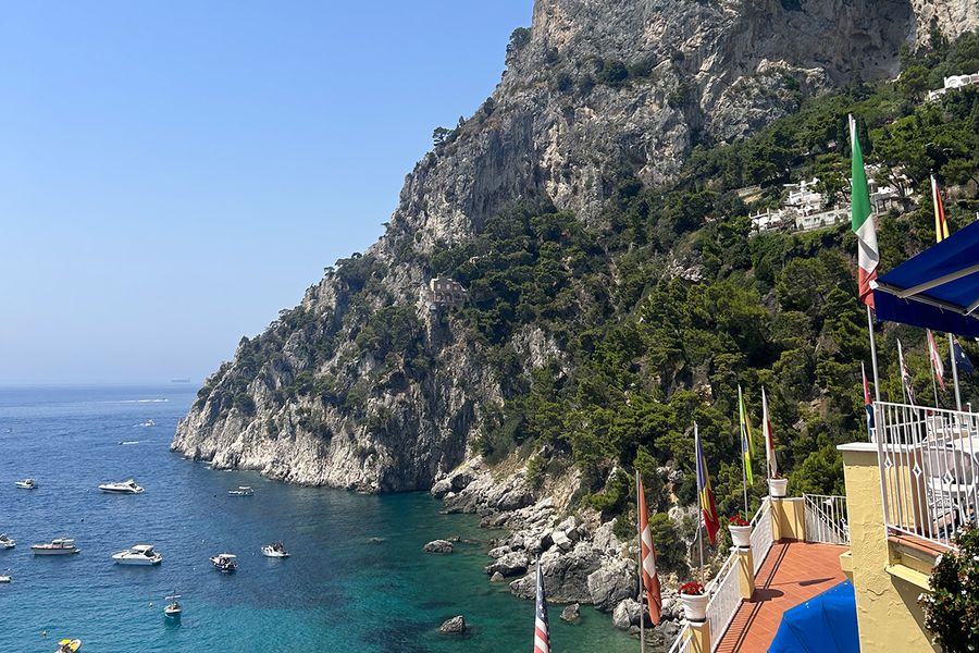 A Mediterranean coastline with hills meeting a blue sea dotted with boats, seen from a balcony in the foreground, capturing the charm of a September holiday in Europe.