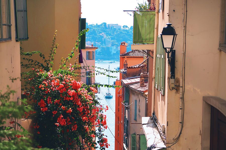 A narrow street lined with flowers leads towards the sea in Nice, capturing the charm of a South of France September holiday.